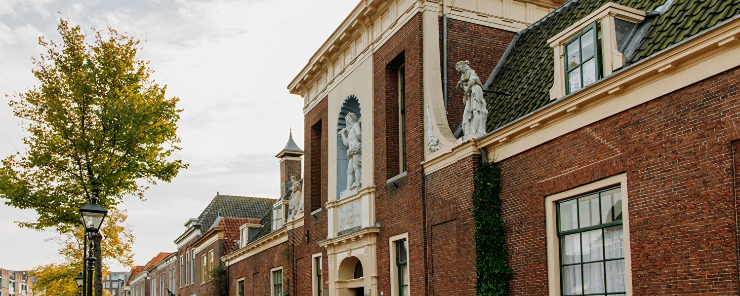 Historisch gebouw in Alkmaar met klassieke beeldhouwwerken en rode bakstenen gevels, gefotografeerd op een rustige straat – headerafbeelding voor het golfarrangement van Amrâth Hotel Alkmaar.