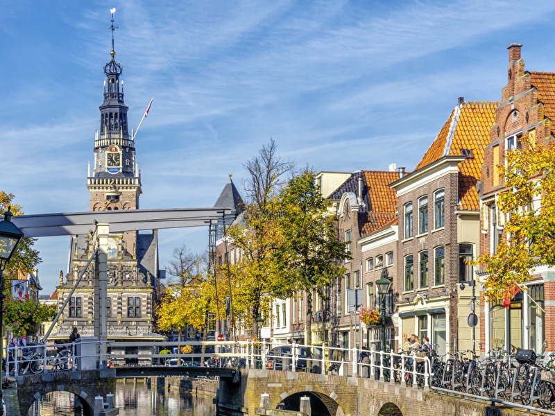 Grote Sint-Laurenskerk en brug over een gracht in Alkmaar. Heldere lucht, herfstbomen, historische gebouwen en een rustige sfeer.